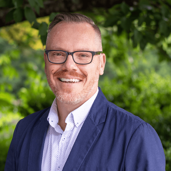 Headshot of Eaton wearing a blue suit in front of a nature background.