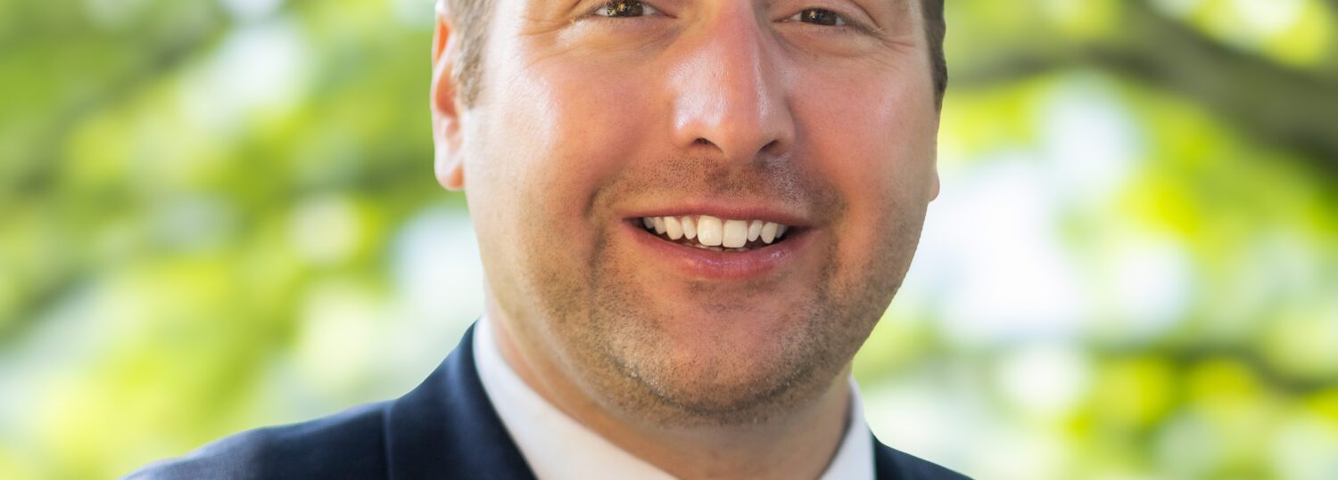 Headshot of Black wearing a black suit and black tie.
