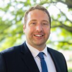 Headshot of Black wearing a black suit and black tie.