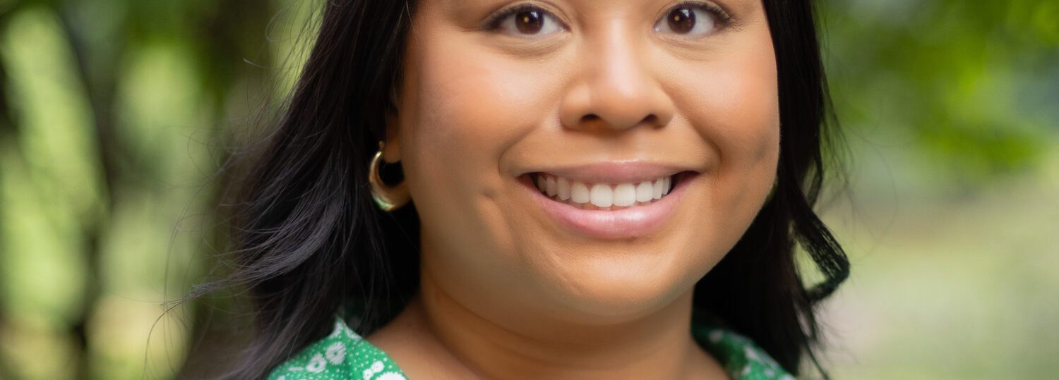 Headshot of Candaso wearing a green patterned dress in front of a natural background.