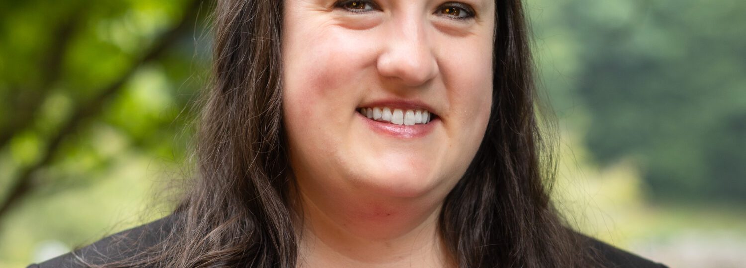 Headshot of Coren wearing a black blazer and a salmon colored shirt.