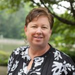 Headshot of Gillespie with a black and white top and a natural background.