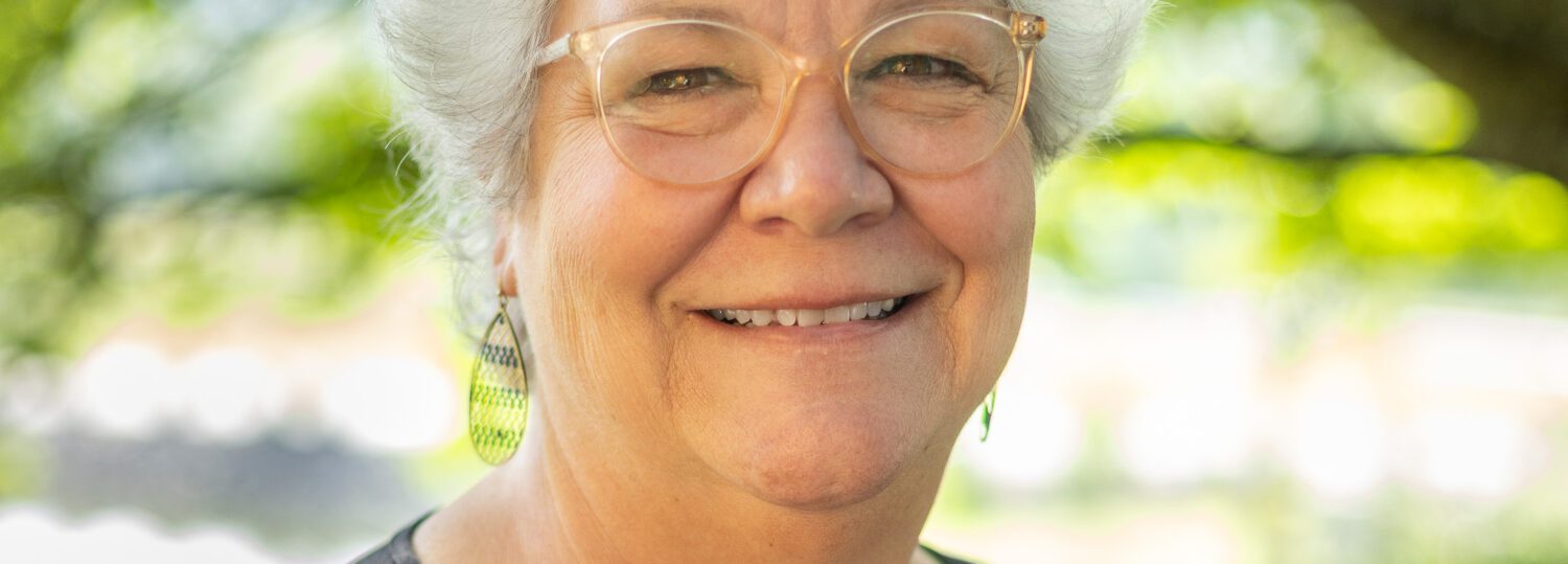 Headshot of Hale with a black top and a natural background.