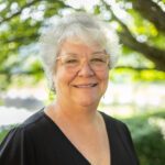 Headshot of Hale with a black top and a natural background.