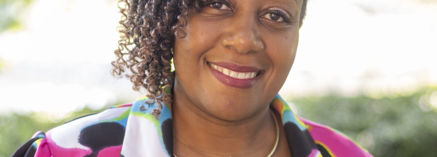 Headshot of Howard wearing a colorful blazer and a flower necklace.