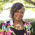 Headshot of Howard wearing a colorful blazer and a flower necklace.