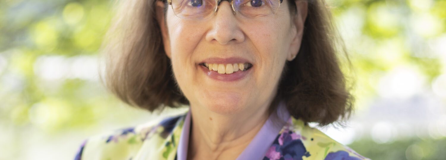 Headshot of Little wearing a colorful blazer over a purple blouse.