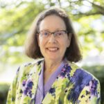Headshot of Little wearing a colorful blazer over a purple blouse.