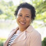 Headshot of Lofters wearing a pale pink blazer over a black and white striped top.