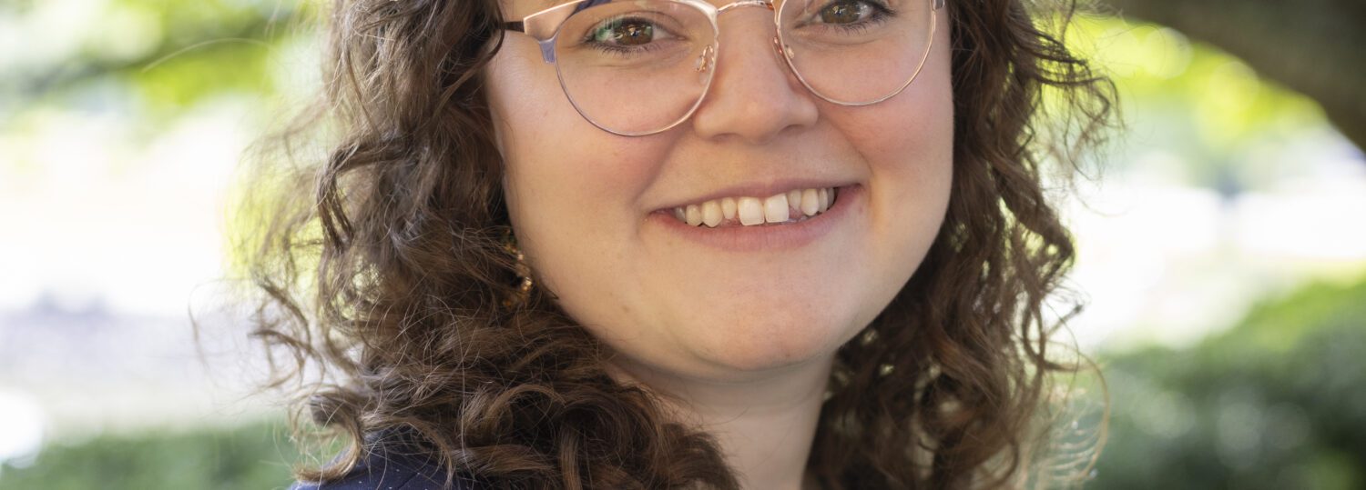 Headshot of Patterson wearing a navy cardigan over a patterned blouse.