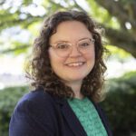 Headshot of Patterson wearing a navy cardigan over a patterned blouse.