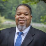 Headshot of Purdie wearing a gray blazer and a blue tie.