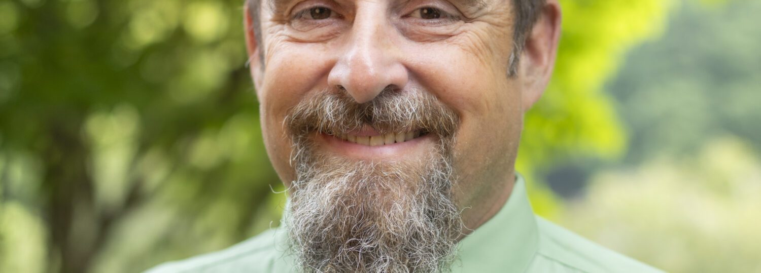 Headshot of Roper wearing a green button up shirt and a tie.