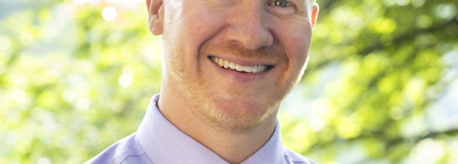 Headshot of Welch wearing a light colored button up shirt with a colorful tie.
