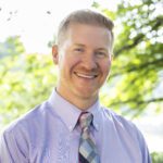 Headshot of Welch wearing a light colored button up shirt with a colorful tie.